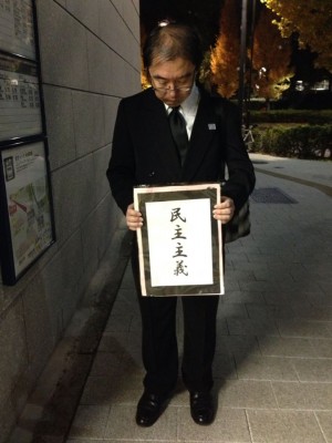 Un hombre sostiene un leterro luctuoso con la palabra "democracia" enfrente del parlamento japonés.